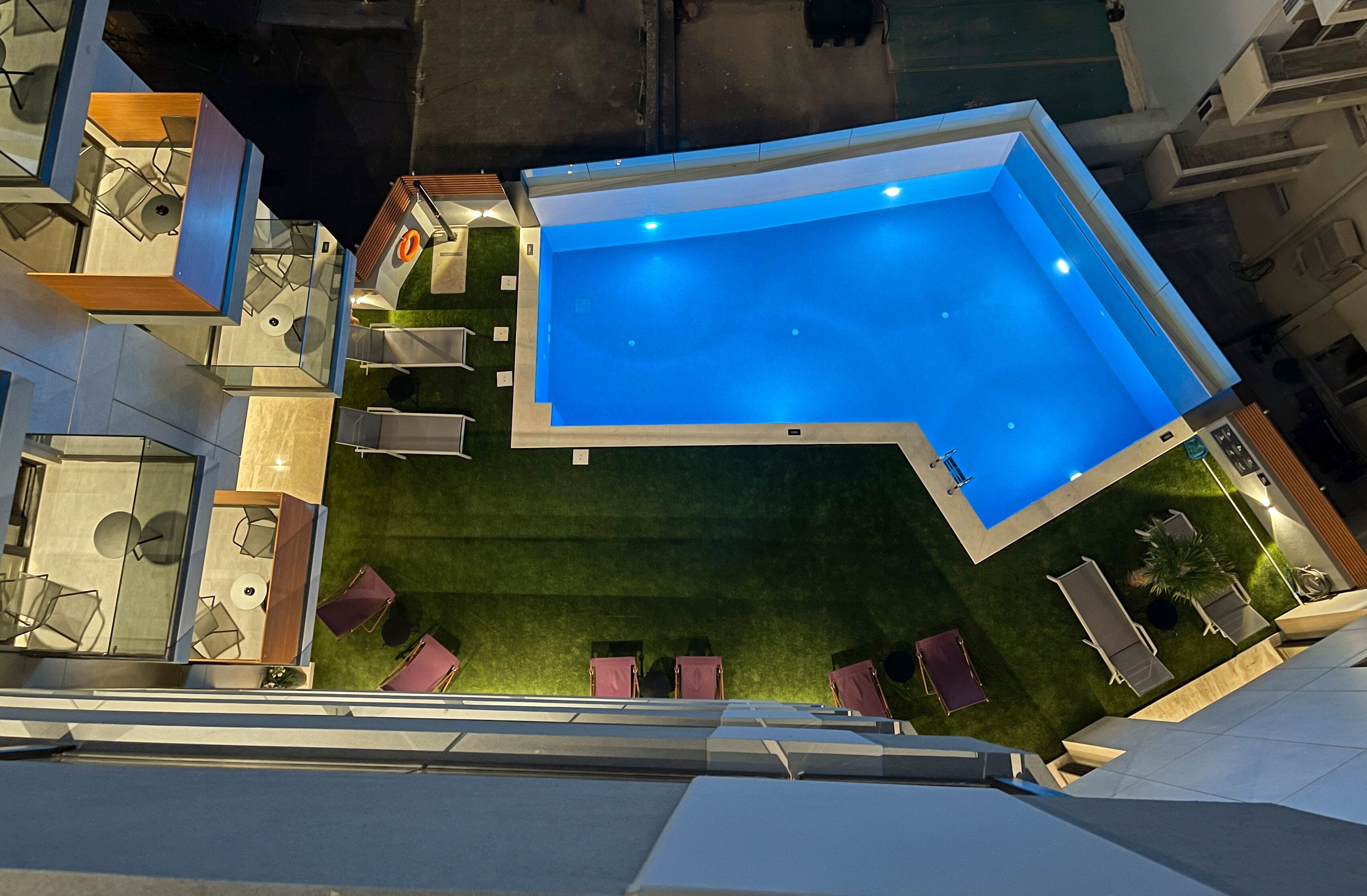 Une piscine extérieure moderne, dotée d’un design géométrique, entourée d’une pelouse bien entretenue et agrémentée de mobilier d’extérieur.