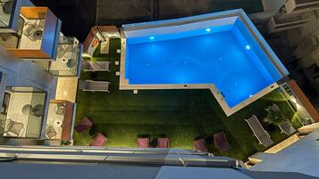 Une piscine extérieure moderne, dotée d’un design géométrique, entourée d’une pelouse bien entretenue et agrémentée de mobilier d’extérieur.