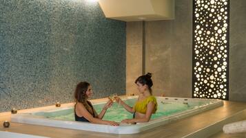 Un grand jacuzzi intérieur avec des murs recouverts de mosaïques et un panneau lumineux décoratif.