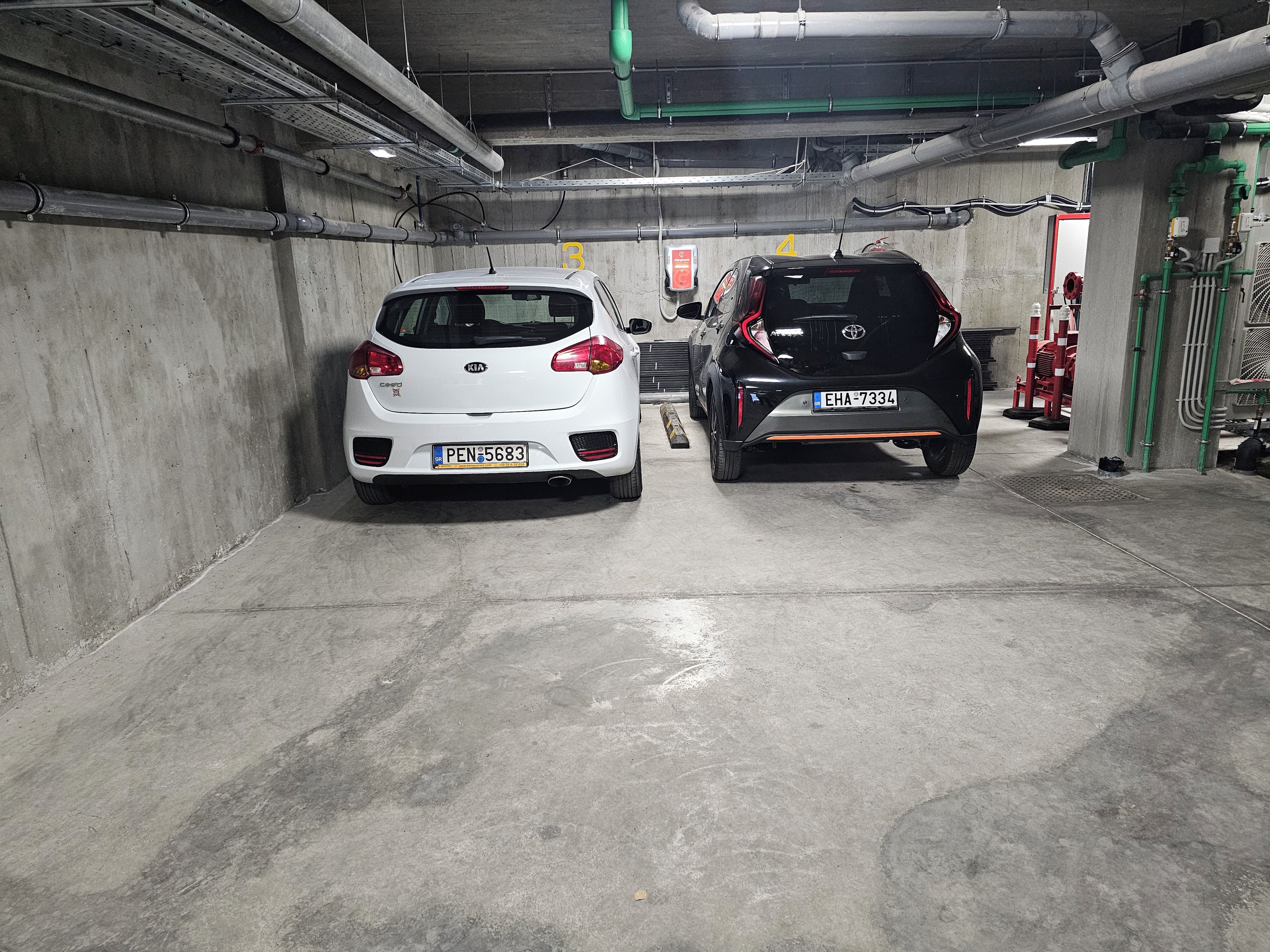 Eine Parkgarage mit zwei Autos, Betonwänden und sichtbaren Rohren.