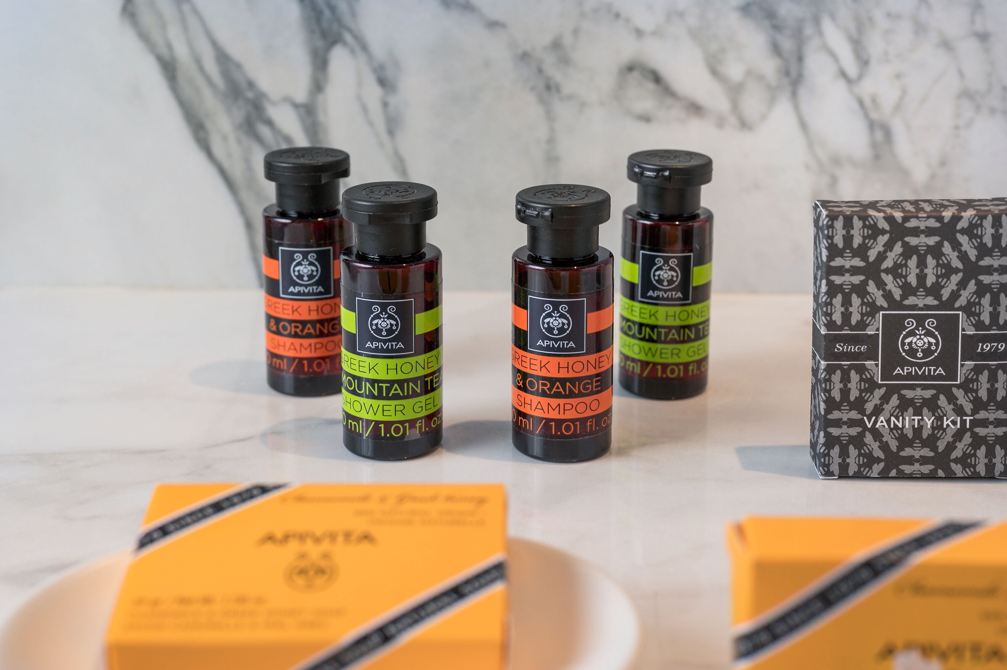 Bottles of APIVITA Greek Honey & Orange Shampoo and Mountain Tea Shower Gel, along with a vanity kit box.