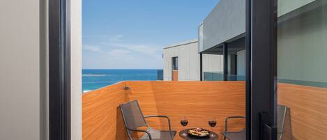 A balcony with a wooden floor, two chairs, a small table, and two glasses of red wine.