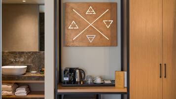 A modern bathroom with a large mirror, a sink, a coffee maker, and a towel rack.