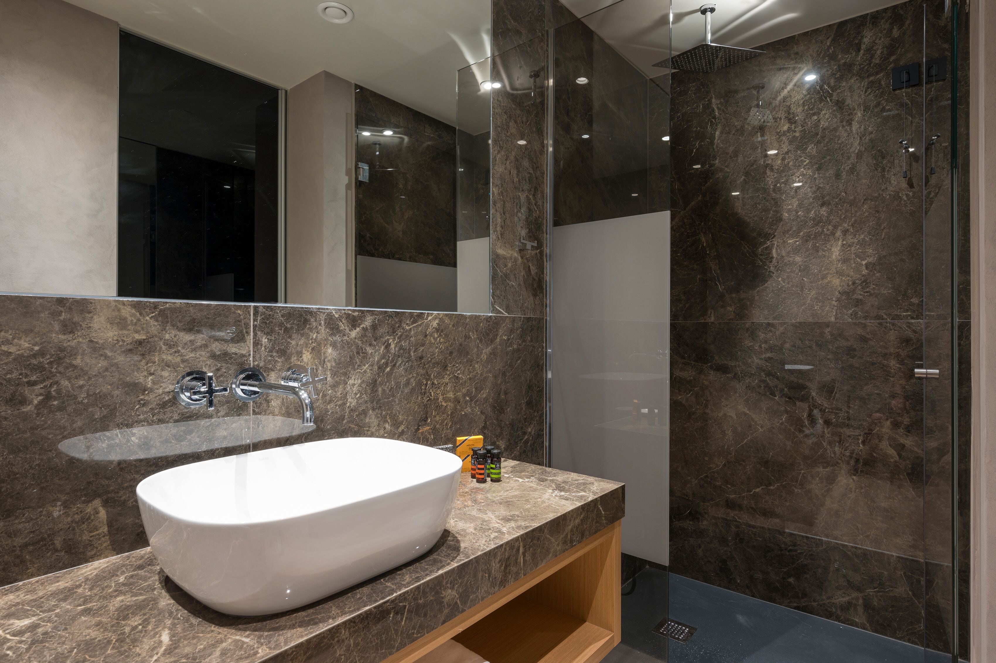 Un baño moderno con un lavamanos grande de color blanco, cabina de ducha de vidrio y paredes de mármol.