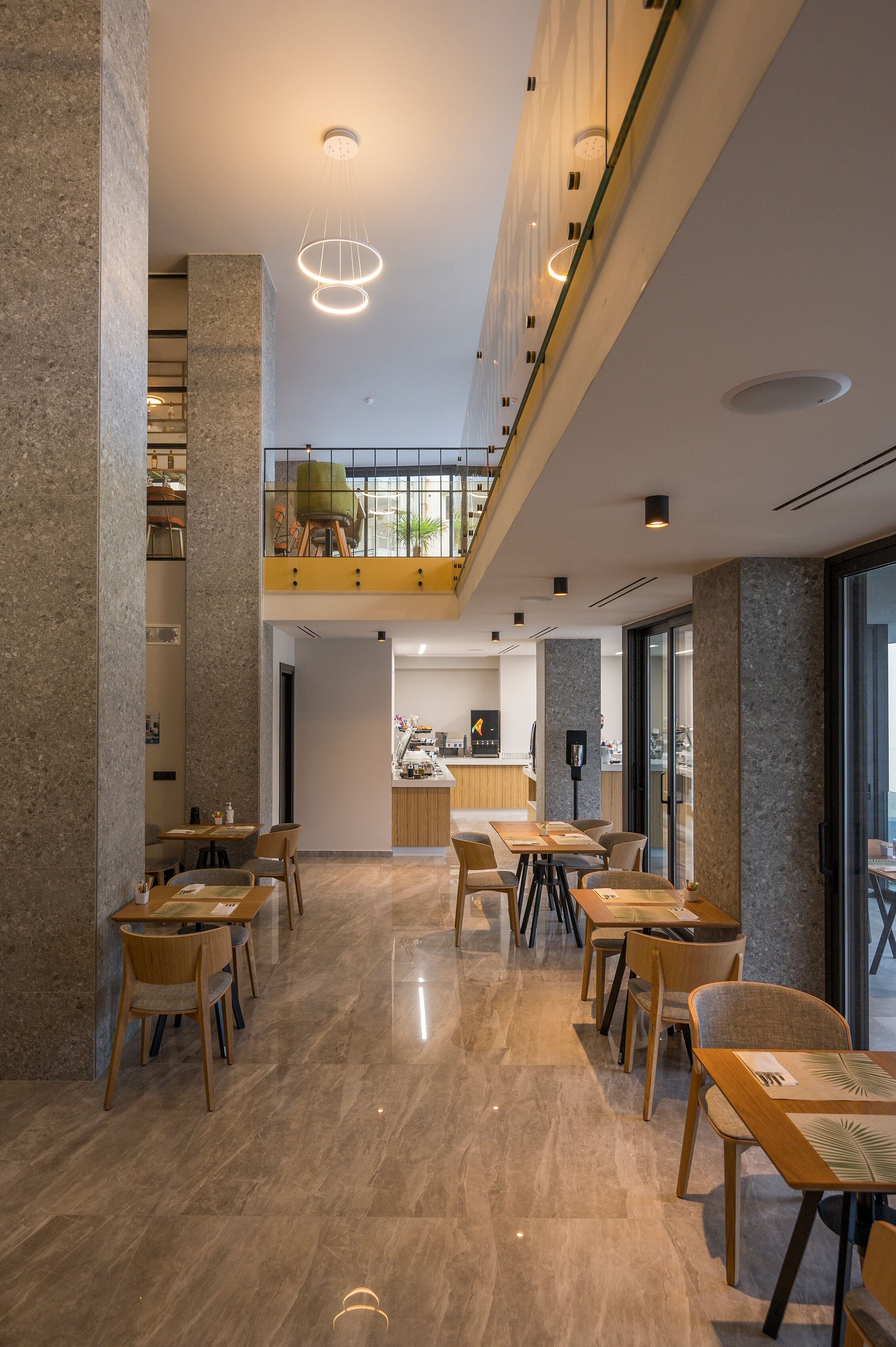 A modern interior with a high ceiling, polished marble floors, and a mezzanine level with seating.