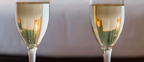 Dos copas de vino blanco sobre una mesa redonda de madera, con un fondo desenfocado de una cama y un cuadro.
