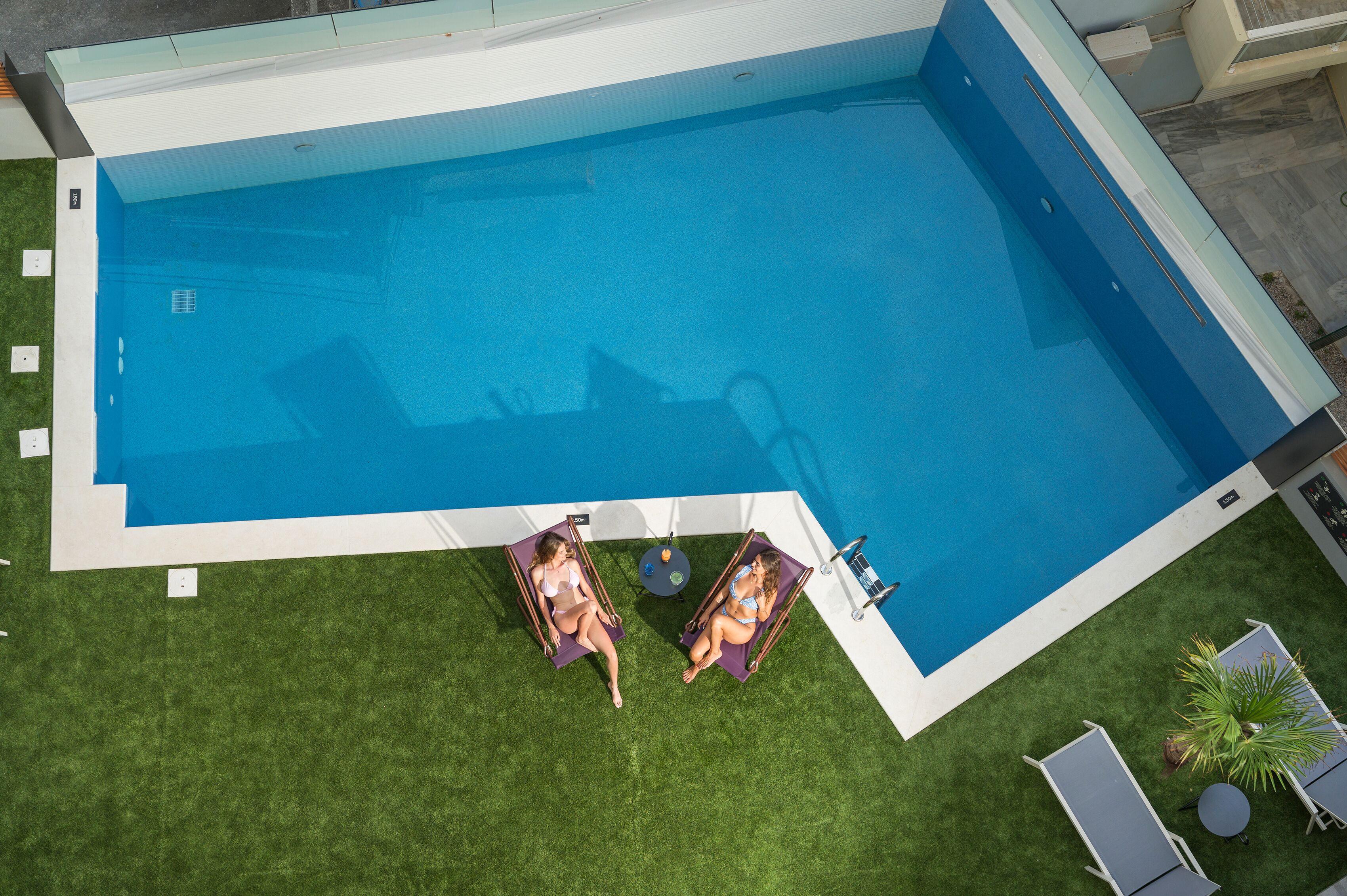 An aerial view of a swimming pool with two lounge chairs and a small table.