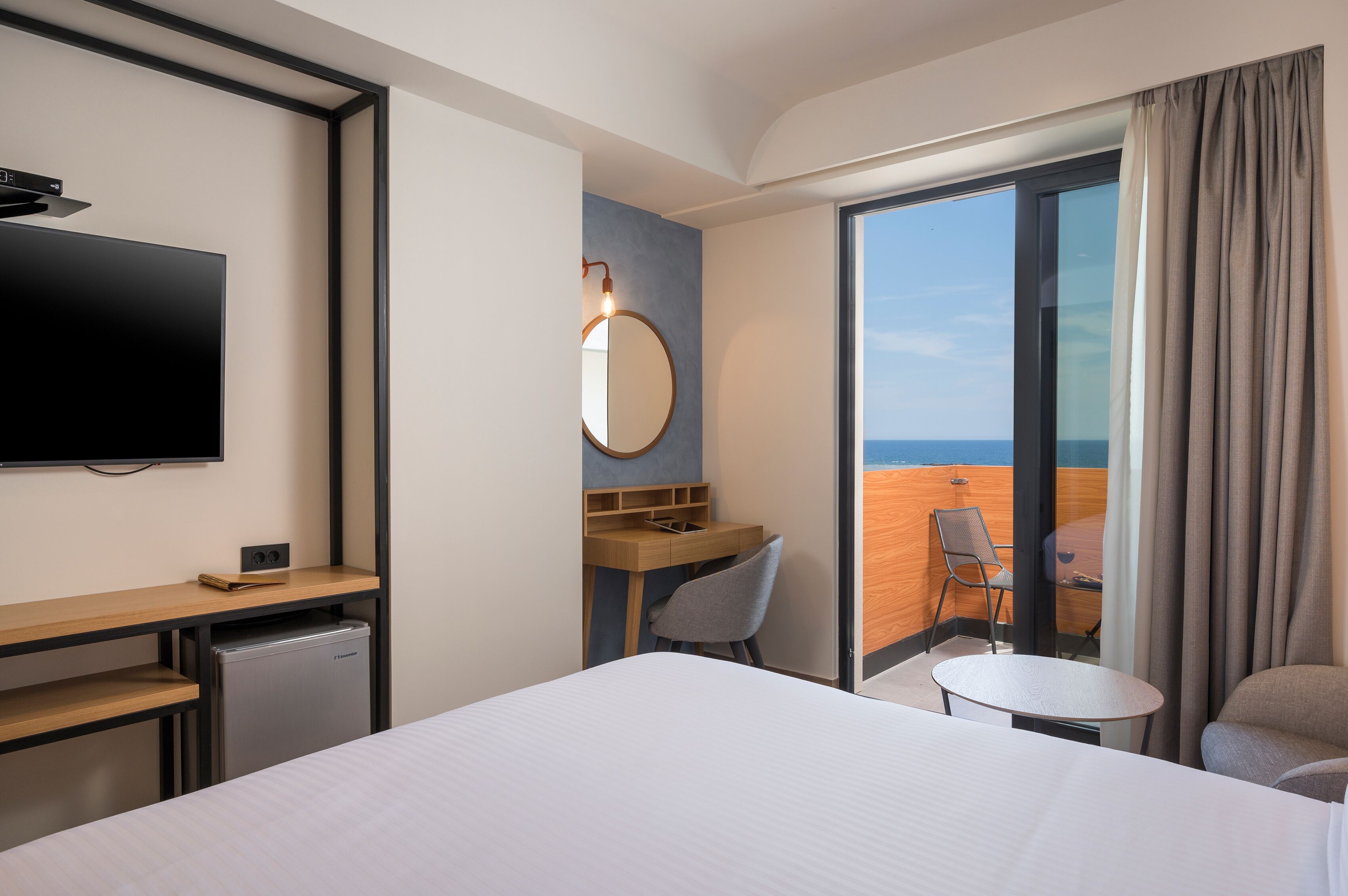 Hotelkamer met een bed, een bureau, een stoel, een kleine tafel, een televisie en uitzicht op de oceaan door een schuifdeur.