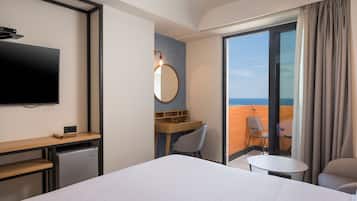 Hotelkamer met een bed, een bureau, een stoel, een kleine tafel, een televisie en uitzicht op de oceaan door een schuifdeur.