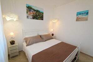 Un dormitorio con cama, mesitas de noche blancas, lámparas de pared y dos carteles con motivos playeros.
