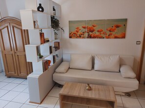 A living room with a white sofa, a wooden coffee table, a bookshelf, and a painting of flowers on the wall.