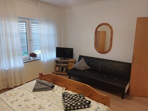 A bedroom with a bed, a black sofa, a television, a wooden door, and a window with curtains.
