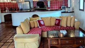 Een ruime woonkamer met een grote beige modulaire bank, een houten salontafel, en een keuken met rode tegels en moderne apparatuur.