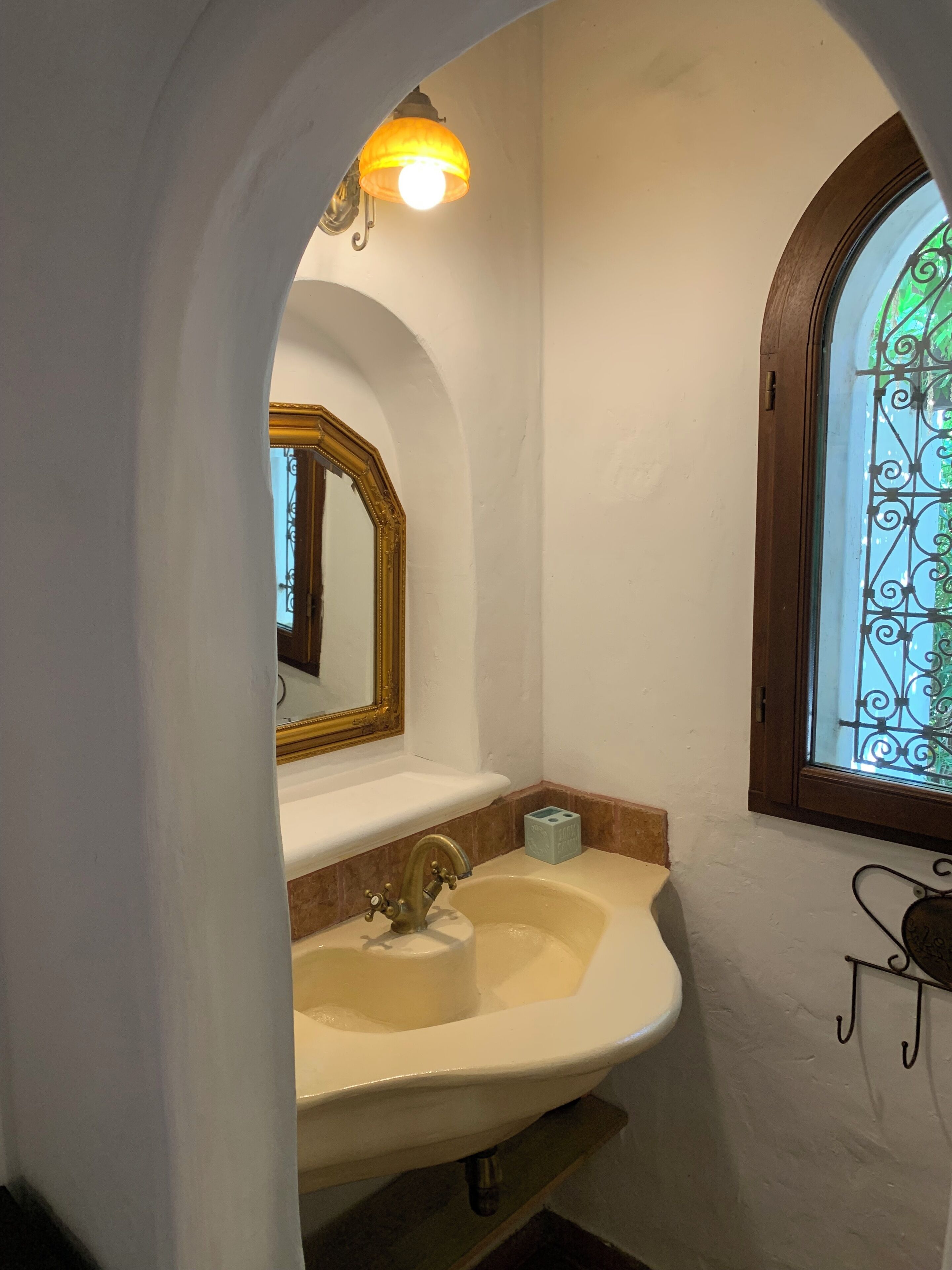 A bathroom with a white sink, a gold-framed mirror, and a window with decorative iron bars.