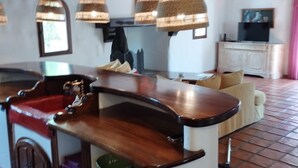 Een keuken met een houten bar, hangende rieten lampen en een betegelde vloer.