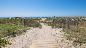 Un sentiero sabbioso che conduce al mare, circondato da dune e recinzioni in legno.