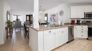 Una cucina moderna con mobili bianchi, un piano di lavoro in granito, elettrodomestici in acciaio inossidabile e un'area pranzo con tavolo e sedie.