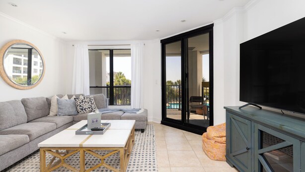 Un soggiorno moderno con divano, tavolino, televisore e un balcone vista piscina.