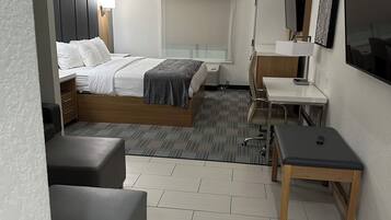 A modern hotel room with a bed, a desk, a chair, a sofa, and a TV.