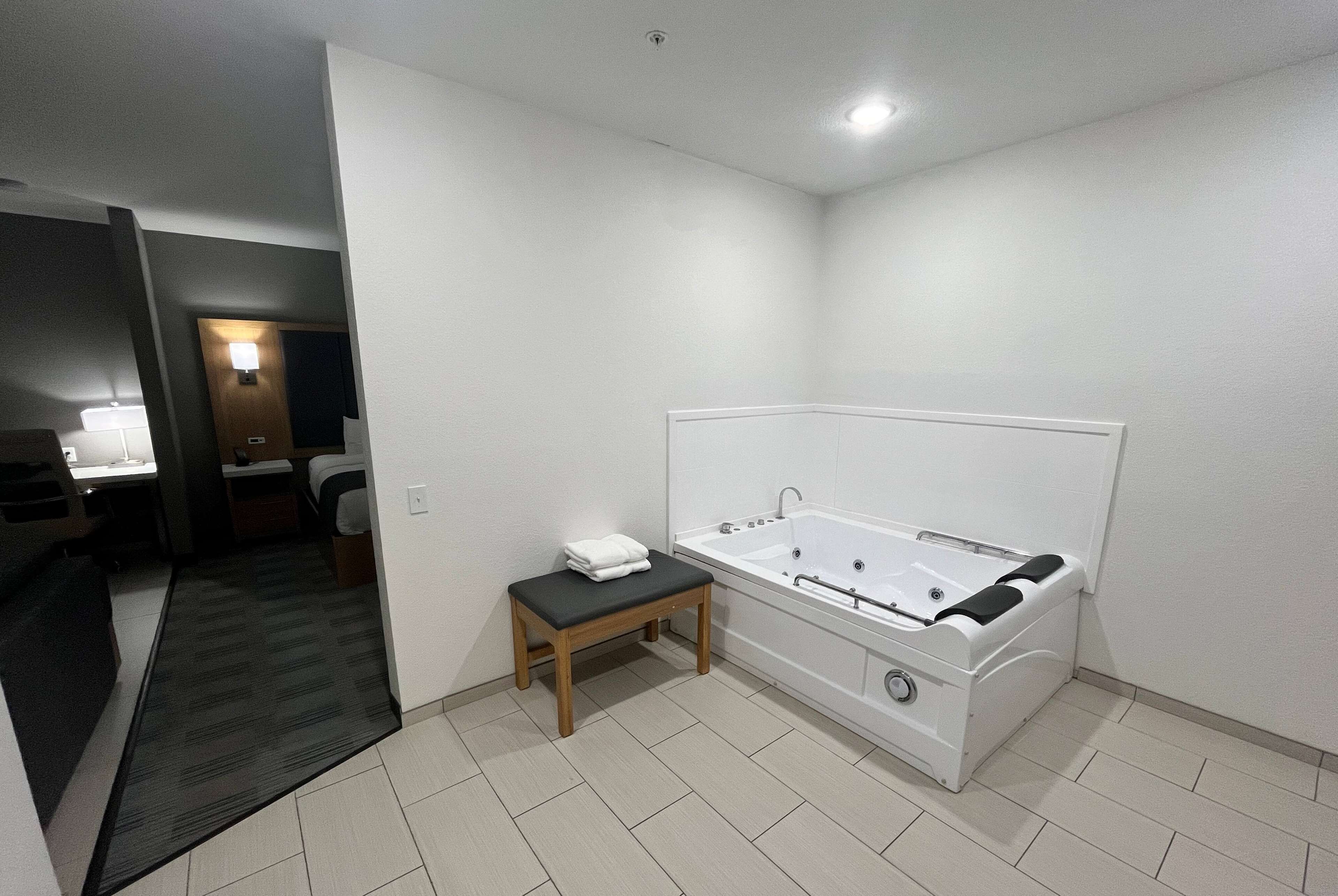 Un baño moderno con una bañera grande, un pequeño banco de madera y un escritorio con una silla.