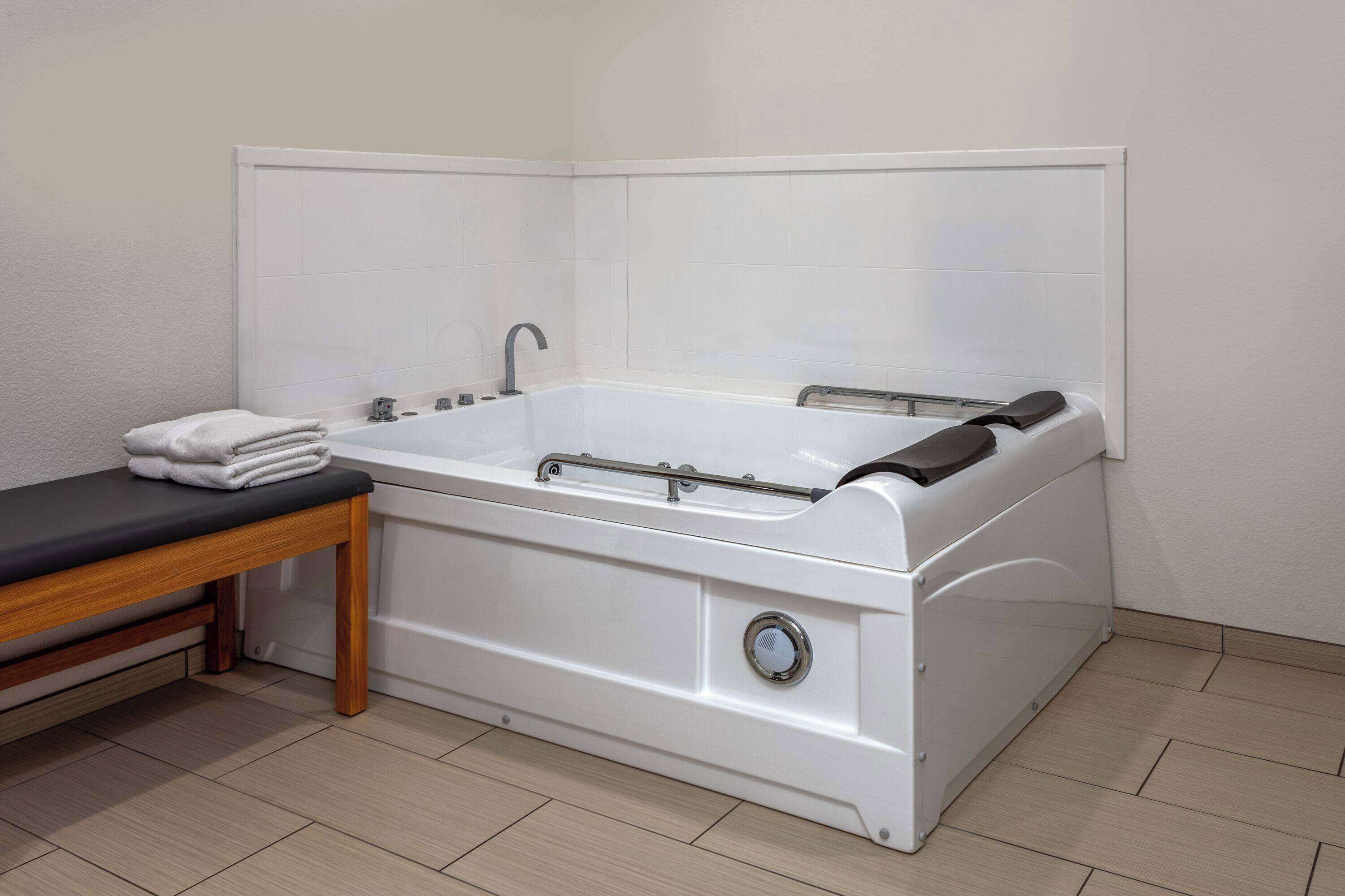 A modern bathroom with a white bathtub, a wooden bench, and a towel on the bench.