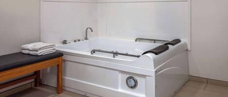 A modern bathroom with a white bathtub, a wooden bench, and a towel on the bench.