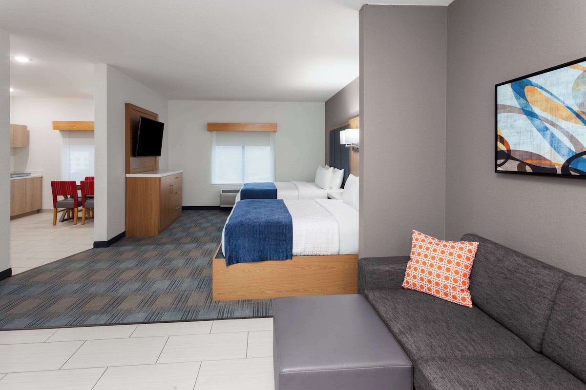 Habitación de hotel con cama, sofá, televisión, escritorio y zona de comedor.