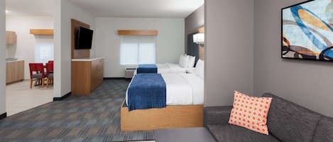 Habitación de hotel con cama, sofá, televisión, escritorio y zona de comedor.