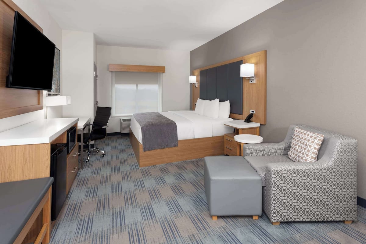 Habitación de hotel con cama, mesitas de noche, televisor, escritorio, silla y un sillón estampado.