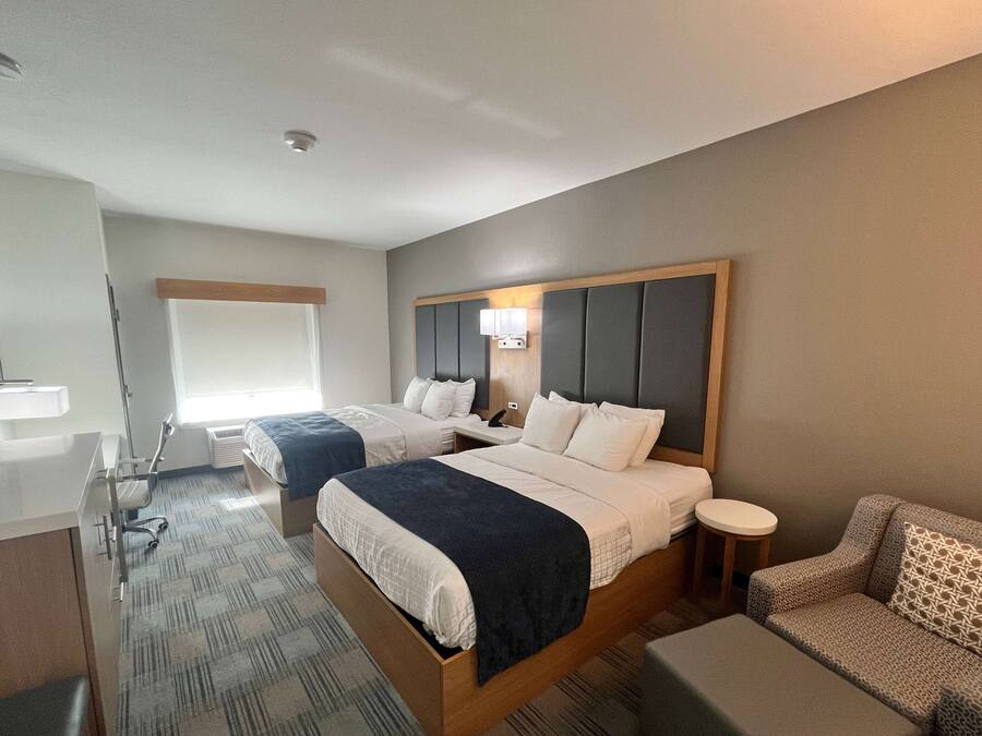 A hotel room with two beds, a desk, a chair, and a sofa.