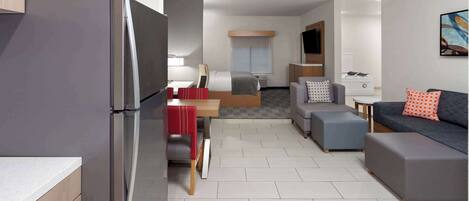 A modern hotel room with a kitchenette, a dining area, a sofa, and a TV.