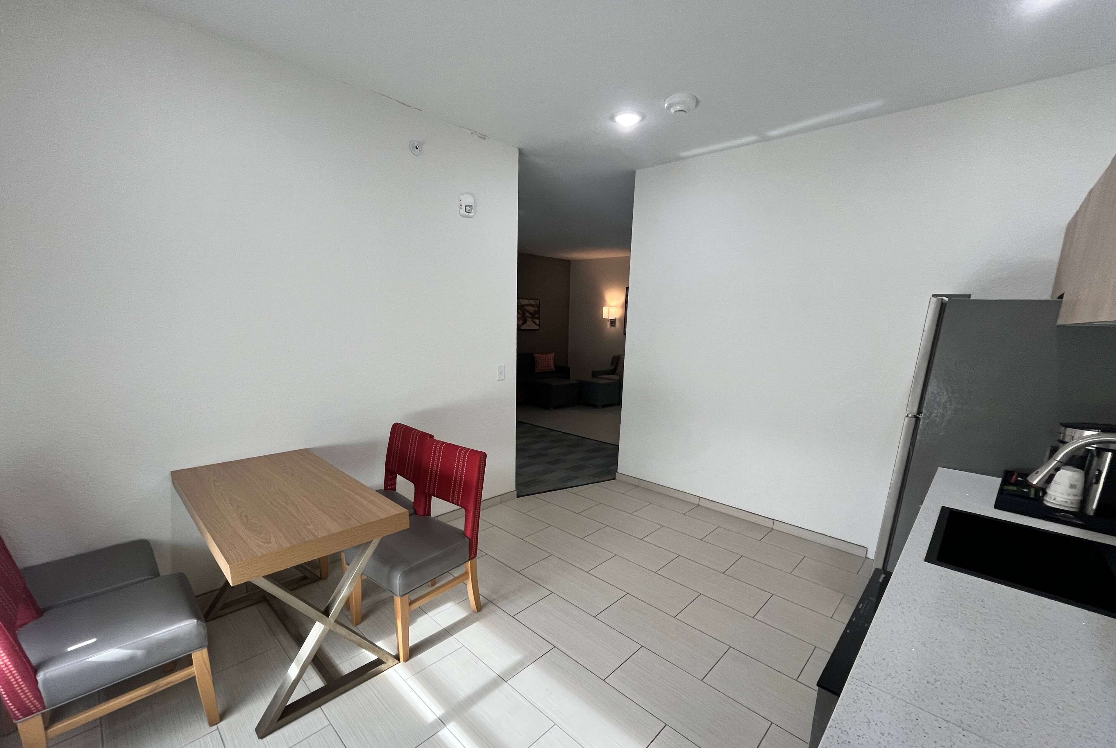 A small, modern kitchen with a countertop and sink, a dining area with a table and chairs, and a visible doorway leading to another room.
