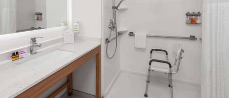 Un baño moderno con ducha, barra de apoyo, inodoro con barra de seguridad y tocador con espejo y lavamanos.