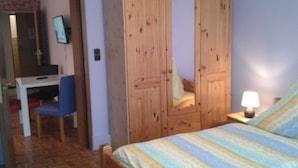 Een slaapkamer met een houten garderobe, een bed met gestreept beddengoed, een bureau met stoel en een lamp op het nachtkastje.