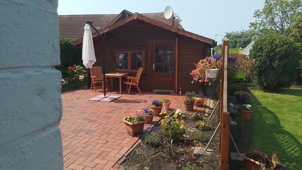 Een houten chalet met een terras, buitenmeubels en bloempotten.