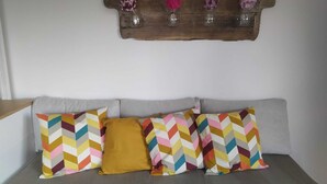 A gray sofa with colorful chevron-patterned pillows and a mustard-colored accent pillow. Above the sofa, there is a wooden shelf with four glass vases containing flowers. - Monolocale La Fornacetta (Pisa)