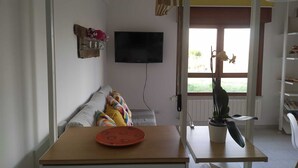 A living room with a sofa, a TV mounted on the wall, a dining table with a plate, and a potted plant. - Monolocale La Fornacetta (Pisa)