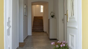 Un pasillo con escalera de madera, paredes blancas y una puerta con picaporte de latón.
