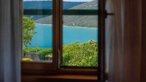 A view through a window of a coastal landscape with a body of water, hills, and a building with a red roof.