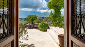 A stone patio with potted plants and a view of the sea.