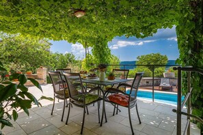 Une terrasse extérieure avec une table et des chaises, une piscine et une vue sur la mer.