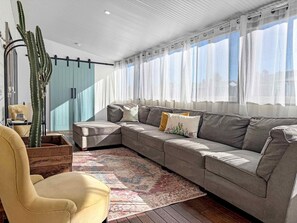 Una sala moderna con un sofá seccional, un sillón amarillo, un cactus grande y una alfombra estampada.