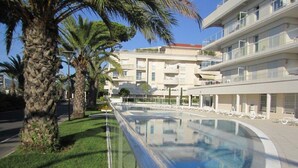 A modern hotel with a swimming pool, palm trees, and a clear sky. - Royal Palm Penthouse (Cannes)