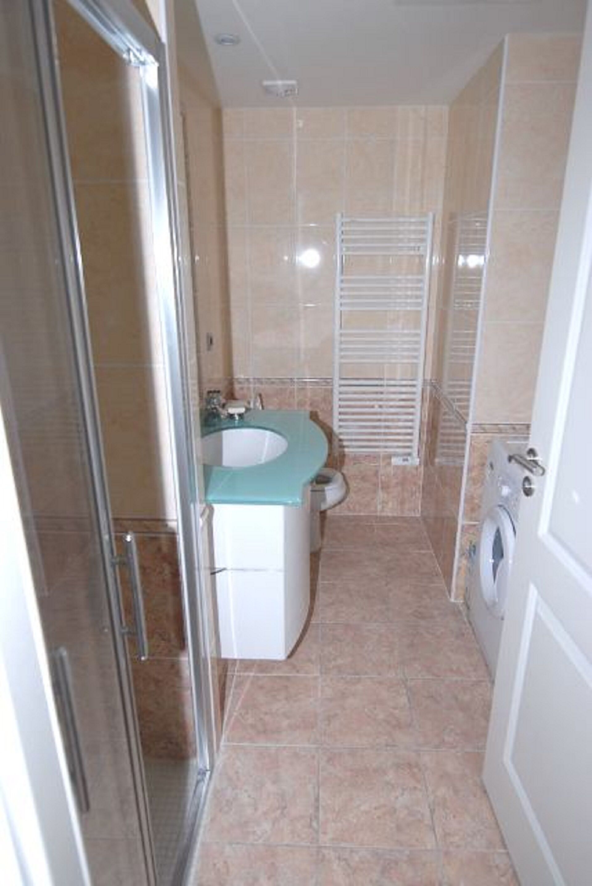 A bathroom with a glass shower enclosure, a sink with a white countertop, and a washing machine.