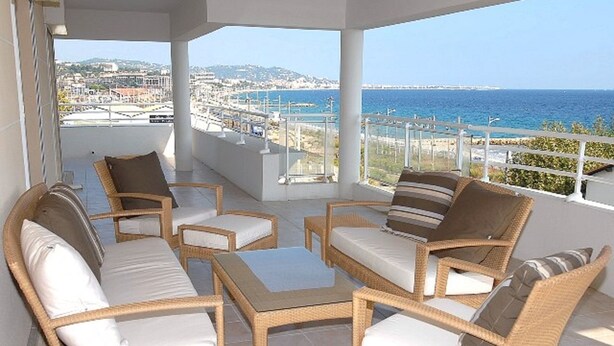 A balcony with wicker furniture, a view of the sea, and a distant cityscape. - Royal Palm Penthouse (Cannes)