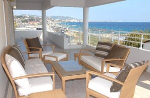 A balcony with wicker furniture, a view of the sea, and a distant cityscape. - Royal Palm Penthouse (Cannes)