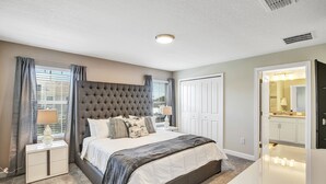 Een slaapkamer met een groot bed, een nachtkastje, een dressoir en een badkamer die door een open deur zichtbaar is.