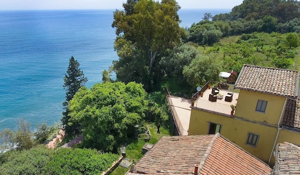 A coastal villa with a terrace overlooking the sea, surrounded by lush greenery.