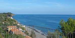 A coastal view with a balcony overlooking the sea, houses along the coastline, and a clear sky.