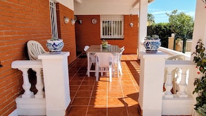 Un patio cubierto con suelo de baldosas, sillas blancas, una mesa y jarrones decorativos.